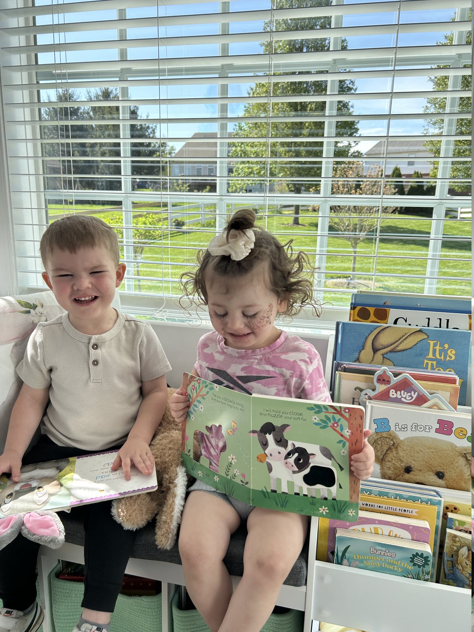 Children smiling while reading books near a sunny window