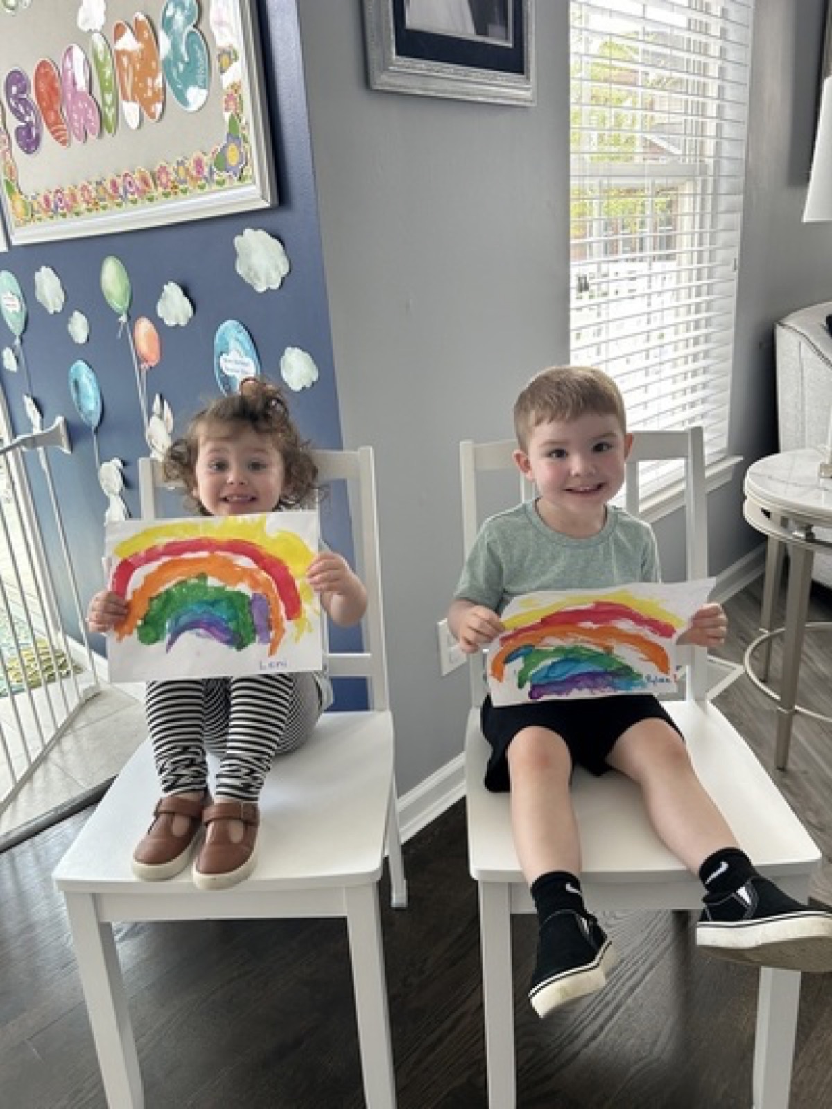 Children holding colorful rainbow paintings