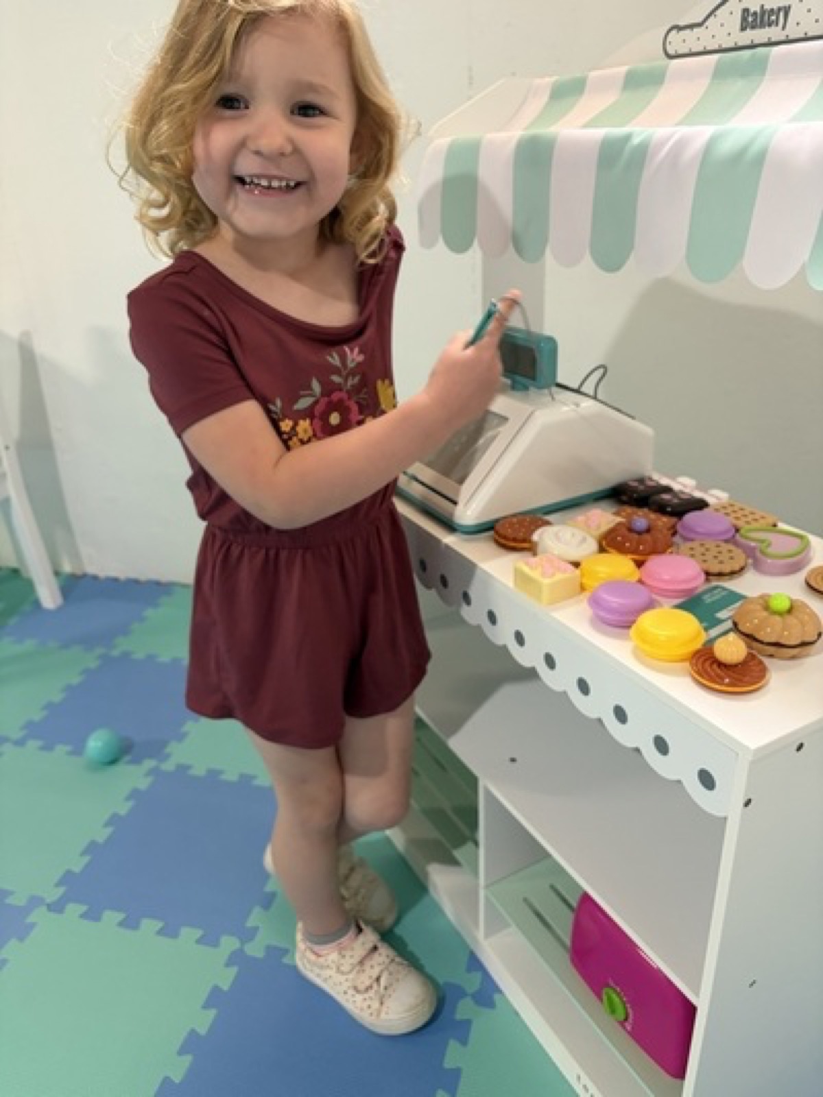 Child playing pretend bakery with toy treats and a register