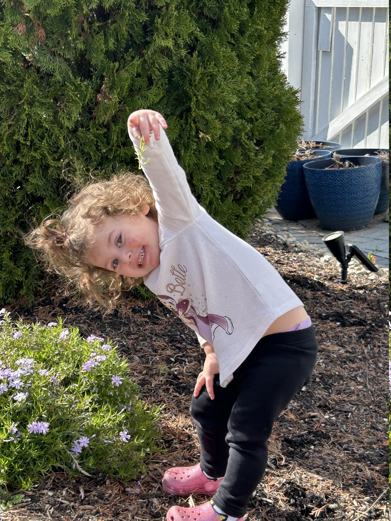 Child smiling outdoors near flowers and shrubs