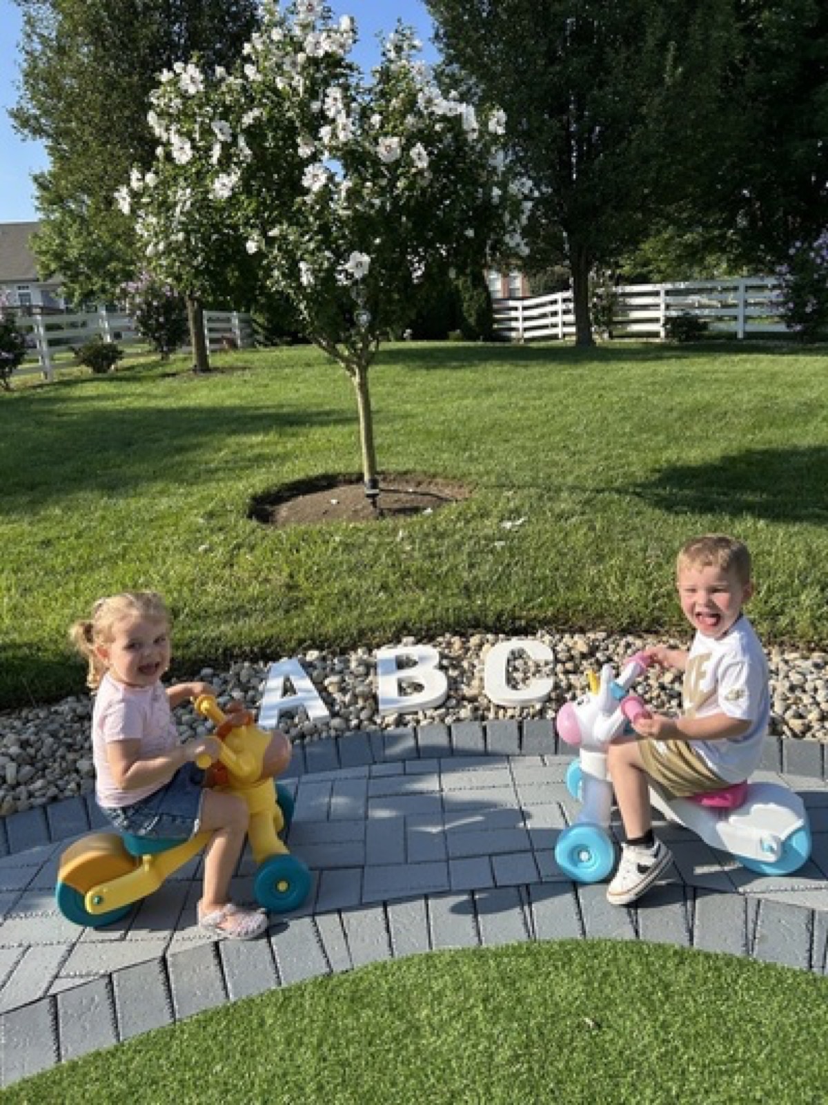 Children riding toys on the outdoor patio near alphabet letters